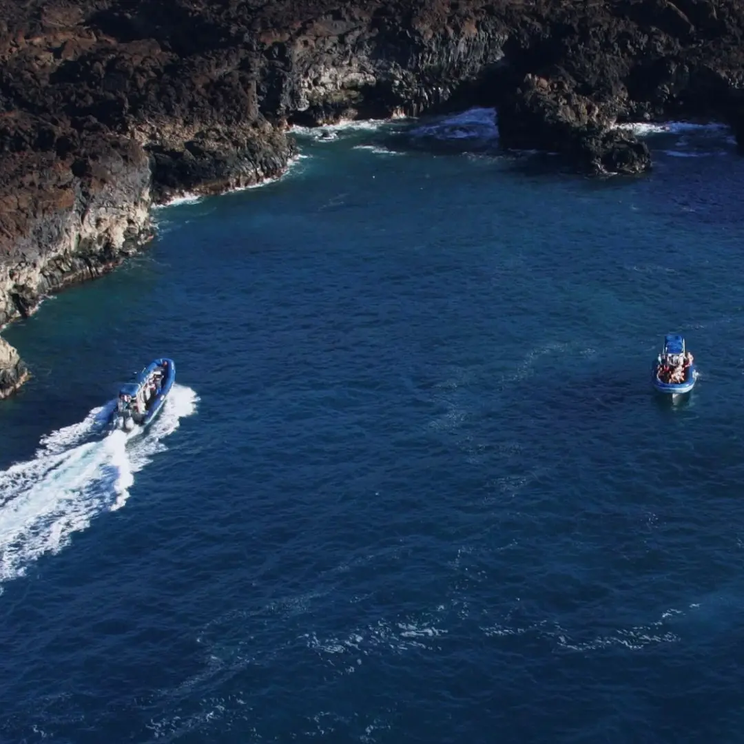 Two tour boats navigate along a rugged coastline with clear blue waters